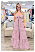 A woman modeling a pink and white vertically striped sleeveless jumpsuit with a large front bow and tiered wide legs, standing in a clothing boutique.