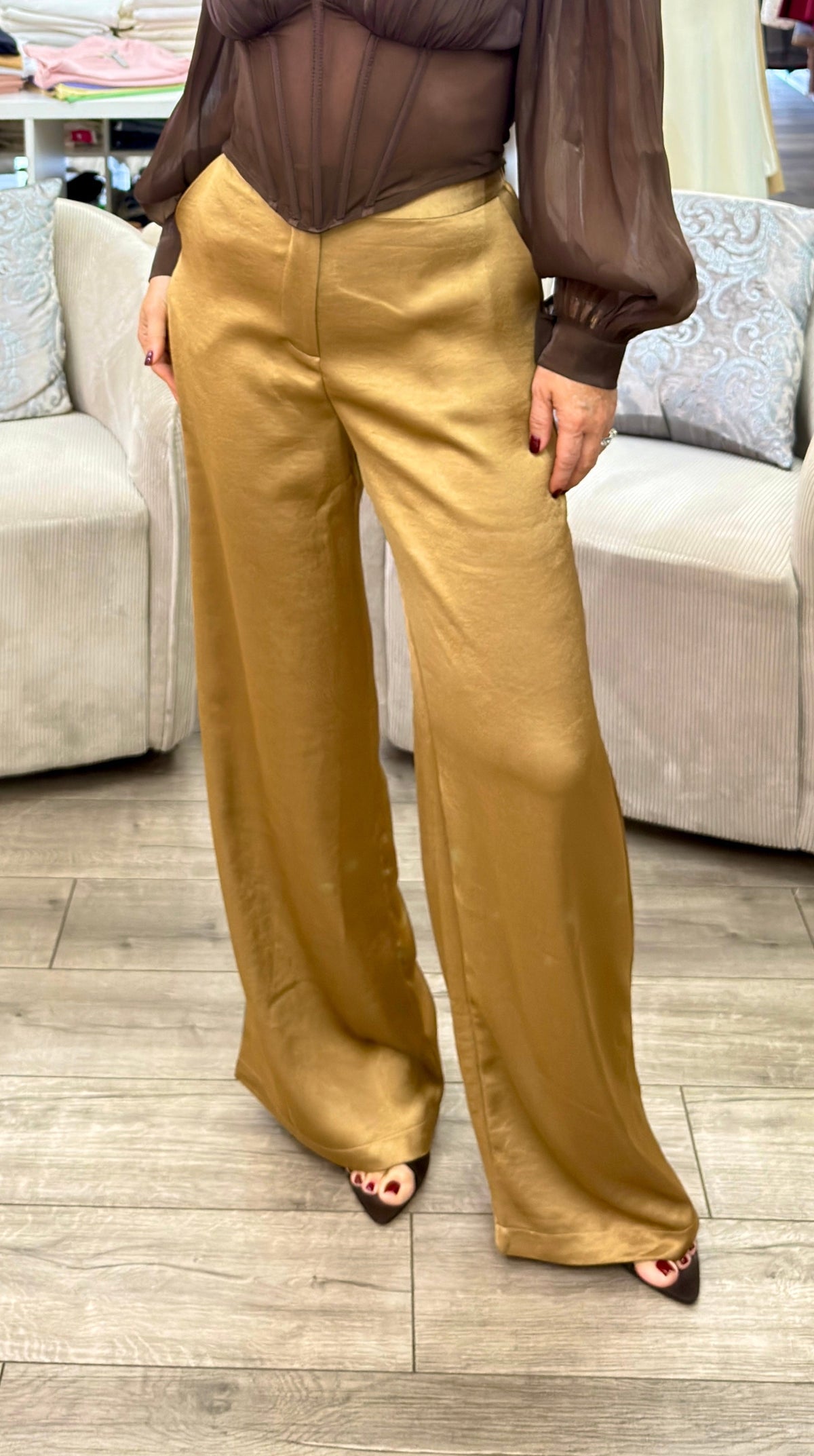 A woman modeling a brown sheer long-sleeve blouse and gold wide-leg trousers in a clothing boutique.
