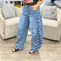 A woman modeling a brown graphic t-shirt and wide-leg light blue jeans with white polka dot side panels, standing in a clothing boutique between two beige armchairs.